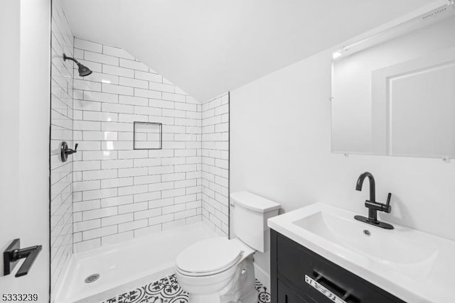 bathroom with toilet, lofted ceiling, tiled shower, and vanity