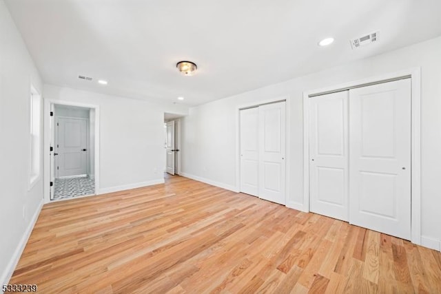 unfurnished bedroom featuring multiple closets and light hardwood / wood-style floors