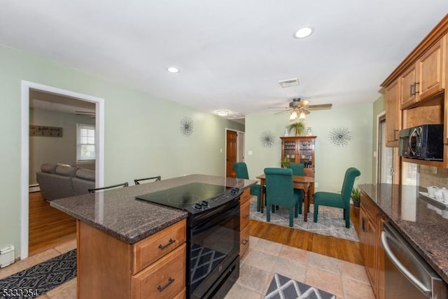 kitchen featuring dark stone countertops, stainless steel dishwasher, a baseboard radiator, ceiling fan, and black range with electric stovetop