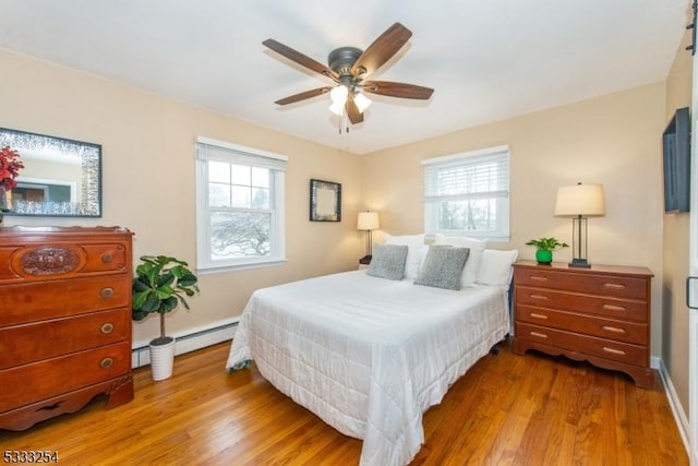 bedroom with a baseboard heating unit, multiple windows, and light wood-type flooring