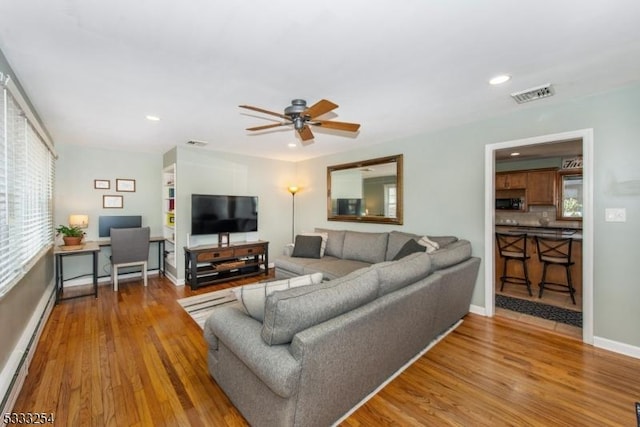 living room with baseboard heating, ceiling fan, and hardwood / wood-style floors