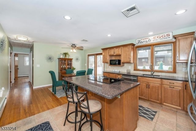 kitchen with sink, black appliances, a kitchen island, dark stone counters, and a baseboard heating unit