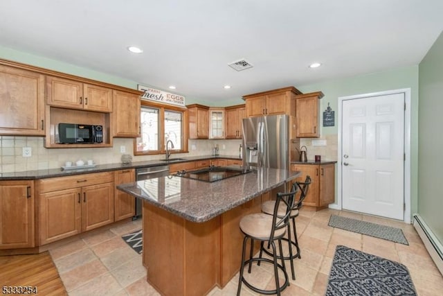 kitchen with a baseboard radiator, sink, dark stone counters, a center island, and black appliances