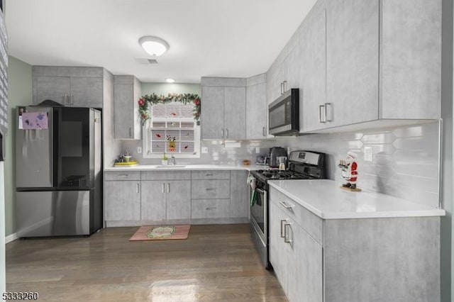 kitchen with tasteful backsplash, gray cabinets, sink, stainless steel appliances, and dark hardwood / wood-style flooring