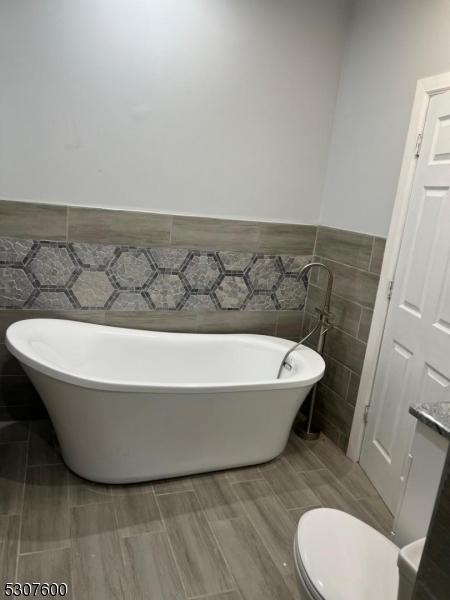 bathroom with tile walls, a bathtub, and toilet