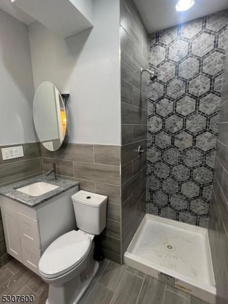 bathroom featuring toilet, a tile shower, tile walls, and vanity