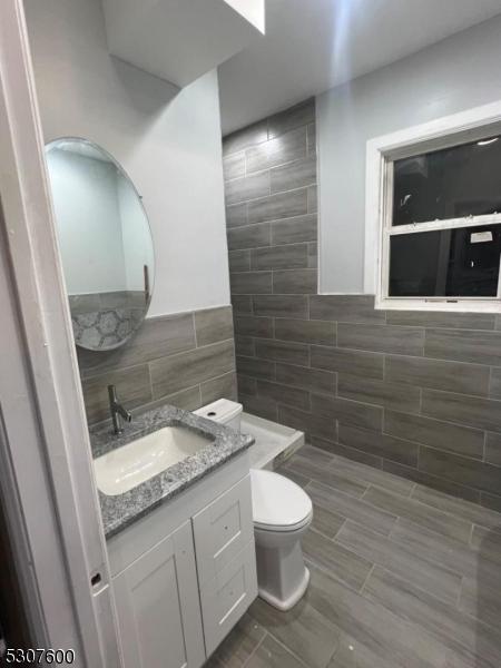 bathroom with toilet, a shower, tile walls, and vanity