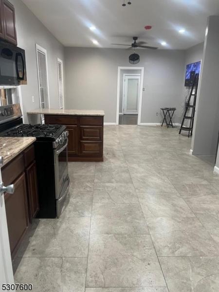 kitchen featuring stainless steel gas stove, light stone counters, dark brown cabinets, and ceiling fan