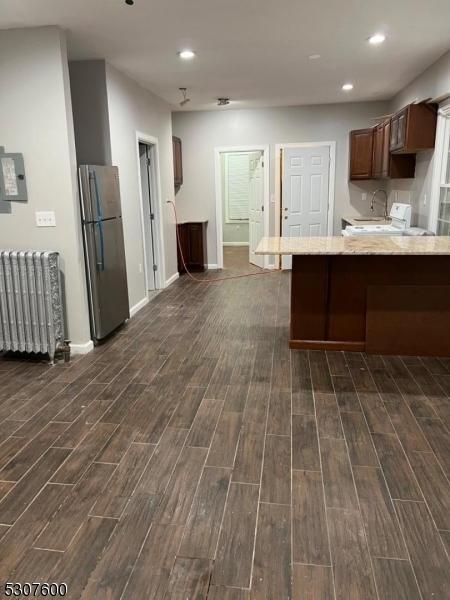 kitchen featuring kitchen peninsula, stainless steel fridge, electric panel, a breakfast bar, and radiator heating unit