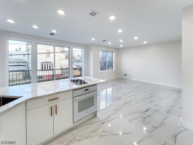 kitchen featuring light stone countertops, white cabinetry, stainless steel gas cooktop, and oven