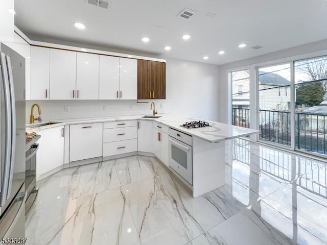 kitchen featuring white cabinets, sink, oven, and stainless steel refrigerator