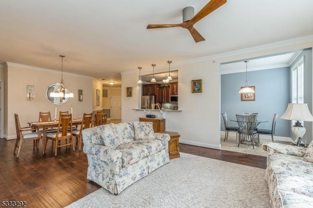 living room featuring dark wood-type flooring, ceiling fan with notable chandelier, and crown molding