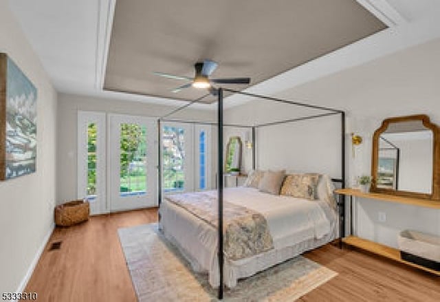 bedroom with ceiling fan, wood-type flooring, a tray ceiling, and access to outside