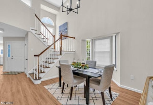 dining room with light wood-type flooring, a towering ceiling, and an inviting chandelier