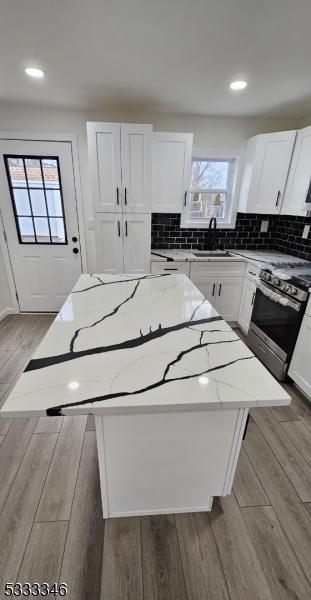 kitchen featuring a kitchen island, white cabinetry, light stone countertops, and sink