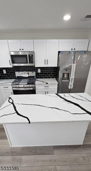 kitchen featuring appliances with stainless steel finishes, white cabinetry, light stone countertops, decorative backsplash, and light wood-type flooring