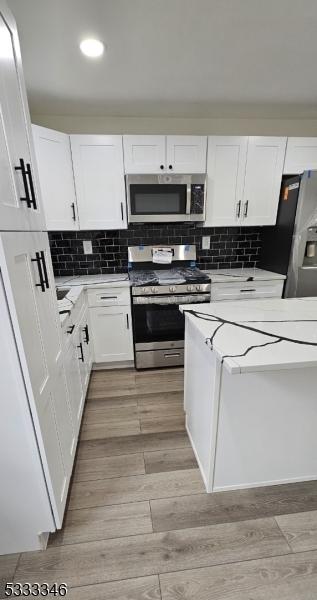 kitchen with white cabinetry, stainless steel appliances, decorative backsplash, and light wood-type flooring