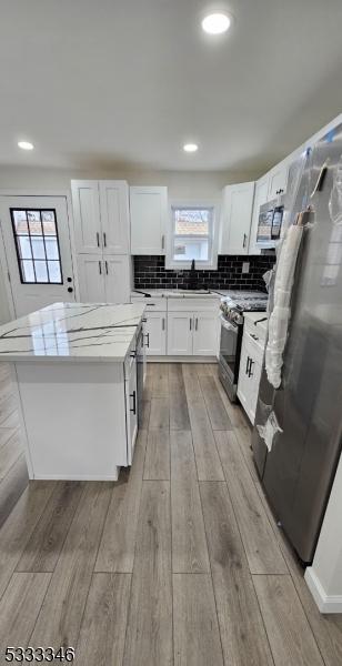 kitchen with tasteful backsplash, a center island, light wood-type flooring, appliances with stainless steel finishes, and white cabinets