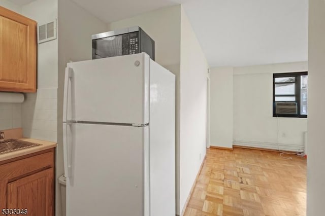 kitchen with light parquet flooring, sink, white fridge, and backsplash