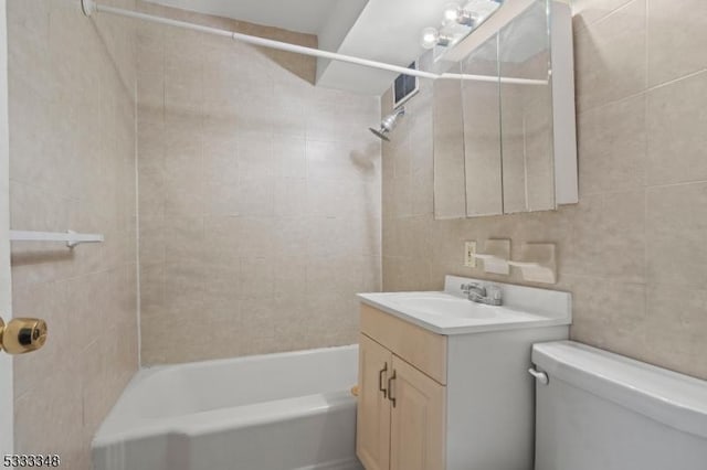 full bathroom featuring vanity, tiled shower / bath, tile walls, and toilet