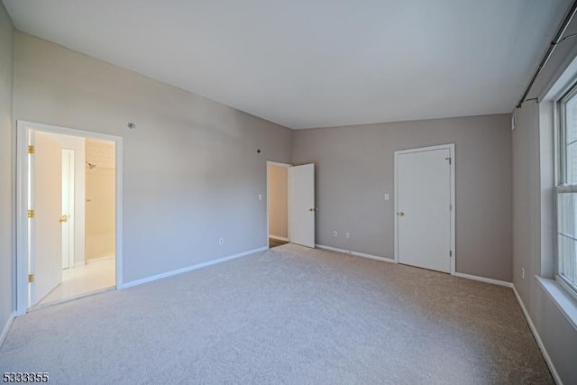 unfurnished bedroom with light carpet, connected bathroom, and multiple windows