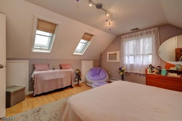 bedroom featuring a wall mounted air conditioner, vaulted ceiling with skylight, and light wood-type flooring