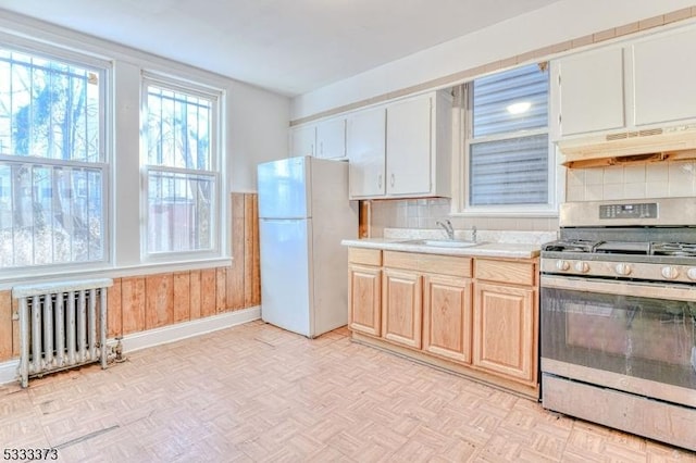 kitchen featuring sink, gas stove, white refrigerator, radiator heating unit, and light parquet flooring