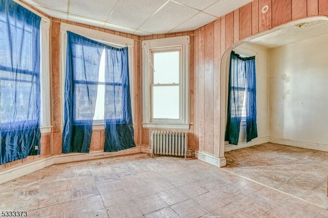 spare room with a drop ceiling, radiator, and wood walls