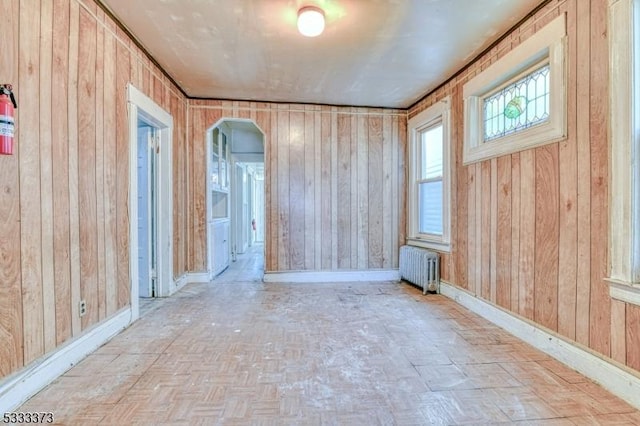 empty room featuring light parquet flooring, radiator heating unit, and wooden walls