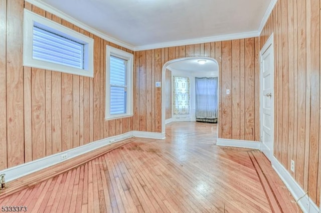 empty room with crown molding, wooden walls, and light hardwood / wood-style flooring