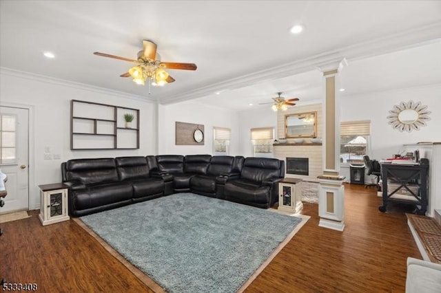 living room featuring dark wood-type flooring, ornamental molding, a large fireplace, and ornate columns