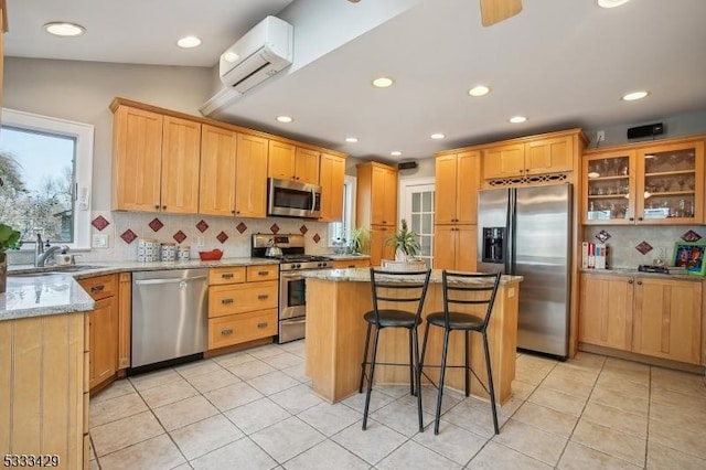 kitchen featuring sink, light stone counters, a center island, appliances with stainless steel finishes, and a wall unit AC