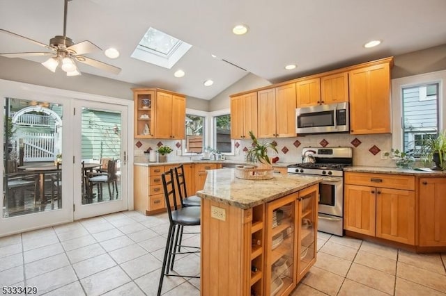 kitchen with light tile patterned flooring, a breakfast bar, light stone counters, appliances with stainless steel finishes, and a kitchen island