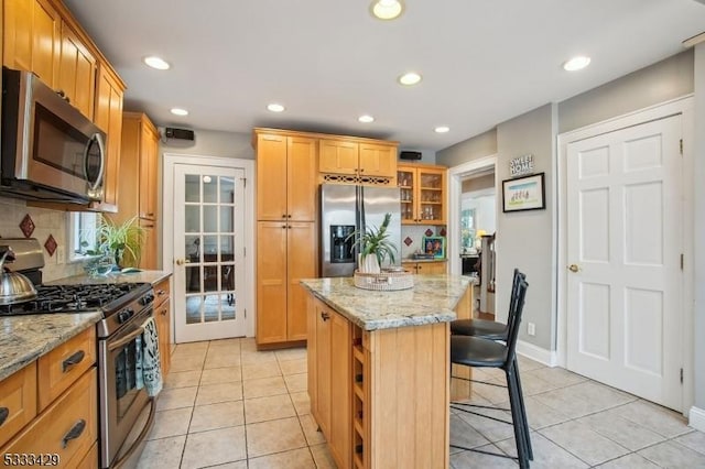 kitchen featuring stainless steel appliances, a kitchen island, light stone counters, and a kitchen breakfast bar