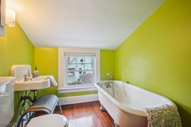 bathroom with hardwood / wood-style flooring, vaulted ceiling, toilet, and a bathing tub