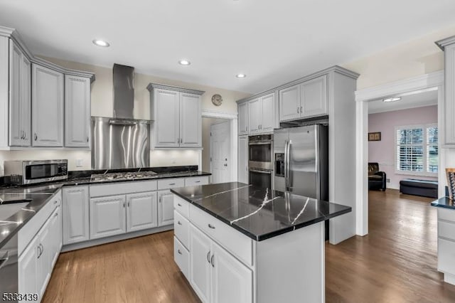 kitchen with hardwood / wood-style floors, appliances with stainless steel finishes, wall chimney range hood, white cabinets, and a center island