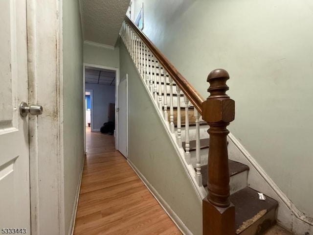 stairway with ornamental molding, hardwood / wood-style floors, and a textured ceiling