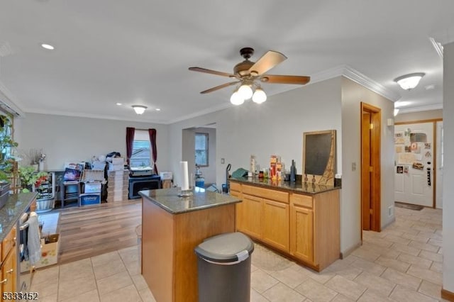 kitchen featuring a center island, dark stone counters, ornamental molding, ceiling fan, and light tile patterned floors