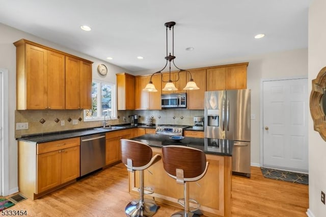 kitchen with decorative light fixtures, light hardwood / wood-style floors, appliances with stainless steel finishes, and a kitchen island