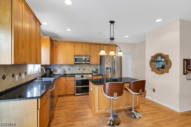 kitchen with appliances with stainless steel finishes, a center island, light hardwood / wood-style floors, sink, and hanging light fixtures