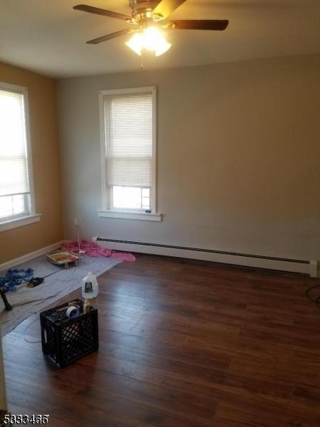 empty room featuring a baseboard heating unit, dark hardwood / wood-style floors, plenty of natural light, and ceiling fan