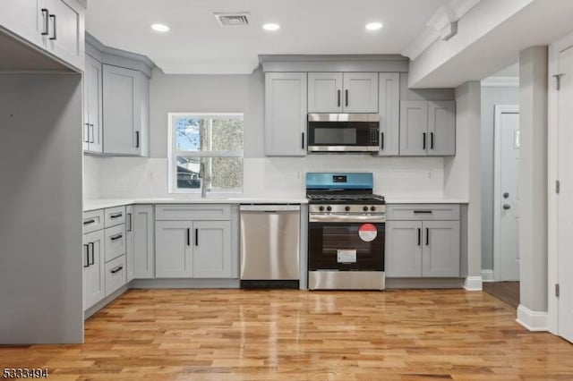 kitchen featuring stainless steel appliances, gray cabinetry, decorative backsplash, and light hardwood / wood-style flooring