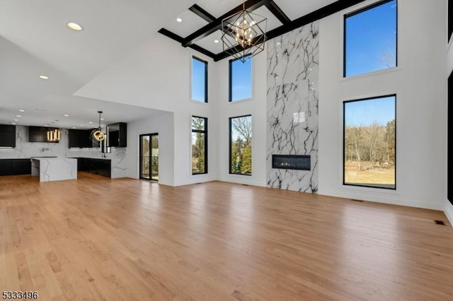 unfurnished living room featuring a fireplace, a towering ceiling, beamed ceiling, light hardwood / wood-style flooring, and a chandelier