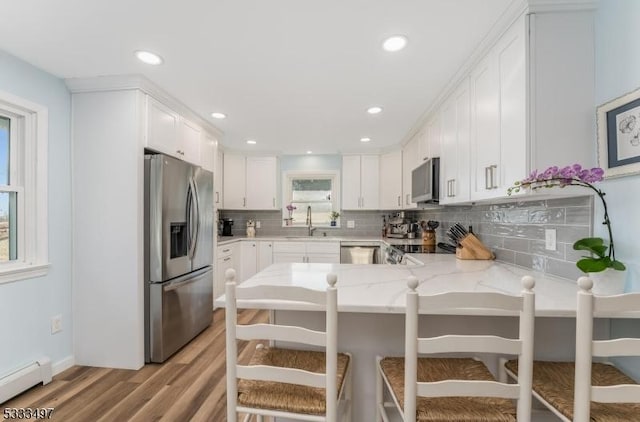 kitchen with white cabinets, stainless steel appliances, kitchen peninsula, and a baseboard radiator