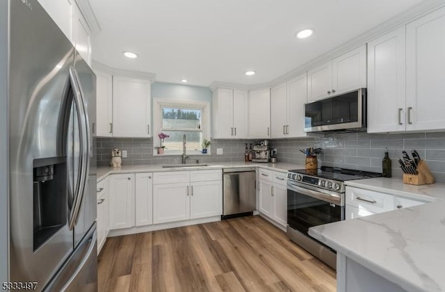 kitchen with light stone countertops, white cabinets, light wood-type flooring, sink, and stainless steel appliances