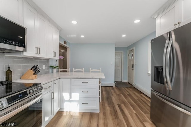 kitchen featuring kitchen peninsula, backsplash, white cabinetry, dark hardwood / wood-style floors, and stainless steel appliances