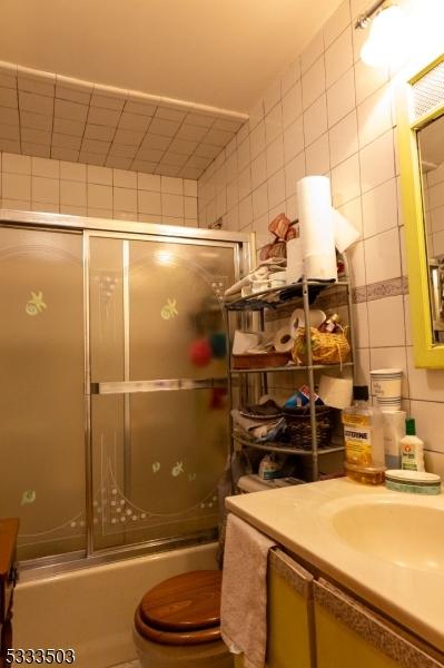 full bathroom featuring vanity, shower / bath combination with glass door, tile walls, and toilet