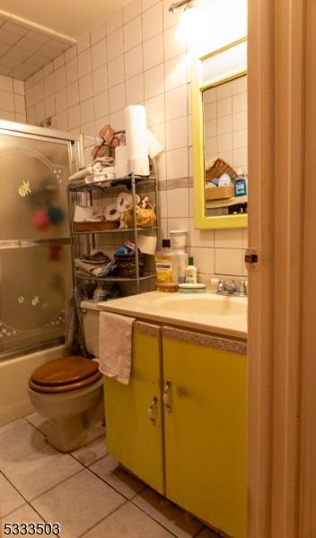 full bathroom featuring tile patterned flooring, tile walls, toilet, shower / bath combination with glass door, and vanity