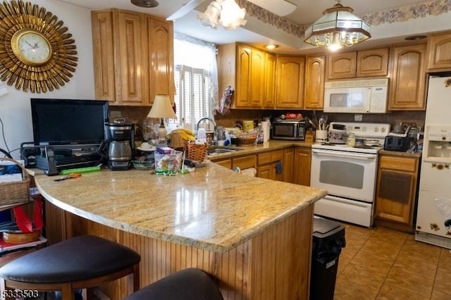 kitchen with kitchen peninsula, sink, light stone counters, white appliances, and a breakfast bar