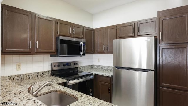 kitchen with sink, tasteful backsplash, stainless steel appliances, light stone countertops, and dark brown cabinetry